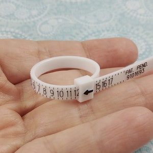 May include: White plastic ring sizer with a black arrow and numbers from 5 to 17. The text "PAT. PEND. 9101693" is printed on the sizer.