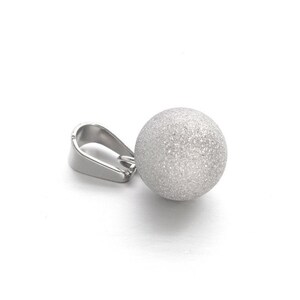 Peut inclure: Un pendentif en argent avec un charme rond en forme de boule texturée. La boule a une finition brillante et givrée.