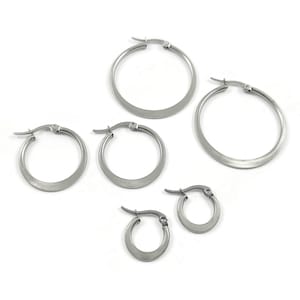 Peut inclure: Ensemble de quatre boucles d'oreilles créoles argentées de différentes tailles. Les boucles d'oreilles sont toutes en métal lisse et brillant.