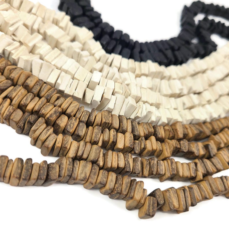 May include: Close-up of several strands of wooden beads in various colors. The beads are square-shaped and strung together. Colors include black, off-white, and shades of brown. The beads are arranged in a curved pattern, suggesting they are part of a necklace or bracelet.