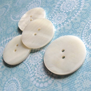 May include: Four white pearl buttons with two holes each. The buttons are arranged in a semi-circle on a blue and white patterned fabric.