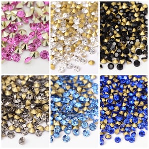 May include: Assortment of colourful rhinestones with gold settings. The rhinestones are in various colours, including pink, clear, black, blue, and grey.