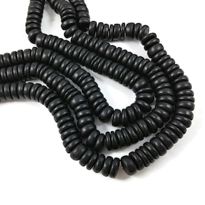 May include: A strand of black wooden beads, each bead is round and slightly flattened, creating a unique texture. The beads are strung together to form a long necklace or bracelet.