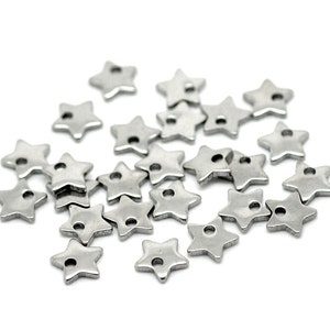 May include: A pile of silver metal star-shaped charms with a hole in the centre. The charms are scattered on a white background.