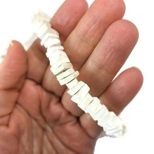 May include: A white beaded necklace with a geometric design. The necklace is composed of small, rectangular beads arranged in a zig-zag pattern. The beads are a creamy white color and appear to be made of a smooth material.
