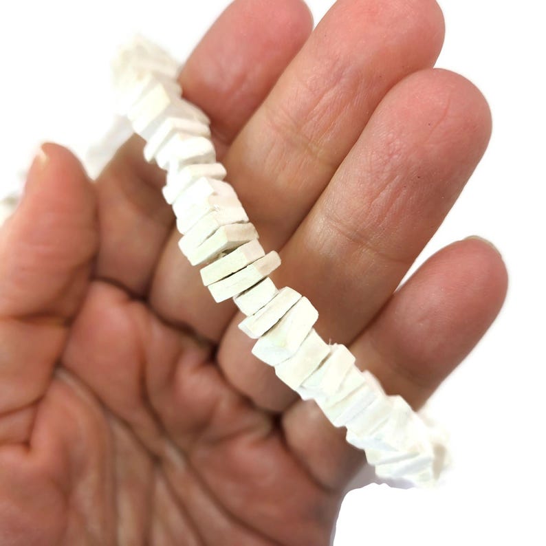 May include: A white beaded necklace with a geometric design. The necklace is composed of small, rectangular beads arranged in a zig-zag pattern. The beads are a creamy white color and appear to be made of a smooth material.