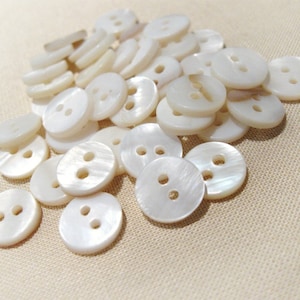 May include: A pile of white, pearl-like buttons with two holes each. The buttons are smooth and have a slight sheen.