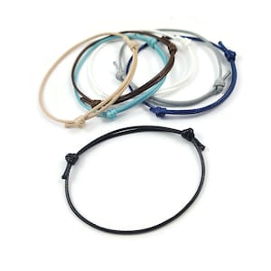 May include: A set of eight colourful string bracelets with adjustable knots. The bracelets are made of thin, braided cord and come in a variety of colours, including black, blue, white, grey, and beige.