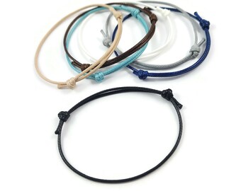 Op de afbeelding: Een set van acht kleurrijke armbandjes van touw met verstelbare knopen. De armbandjes zijn gemaakt van dun, gevlochten koord en zijn verkrijgbaar in verschillende kleuren, waaronder zwart, blauw, wit, grijs en beige.