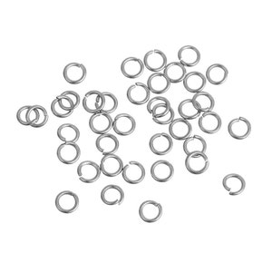 May include: A scattering of small, silver jump rings against a white background. These circular rings have a small gap, likely for joining jewellery components or craft projects. The lighting accentuates the metallic finish of the rings.