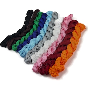 Peut inclure: Une collection de 12 bobines de cordon ciré en coton de différentes couleurs, dont le noir, le vert, le bleu, le gris, le blanc, le rose, le rouge et l'orange. Les cordons sont disposés en éventail, les extrémités se chevauchant.