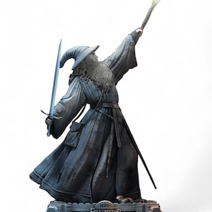 May include: A gray and silver statue of Gandalf the Grey from The Lord of the Rings: The Fellowship of the Ring. He is holding a staff with a glowing tip and a sword. He is wearing a long robe and a pointed hat.
