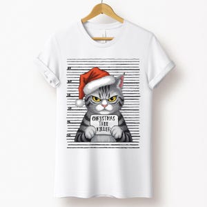 May include: A white t-shirt with a gray cat wearing a red Santa hat and holding a sign that says "Christmas Tree Killer". The cat is in front of a black and white striped background.