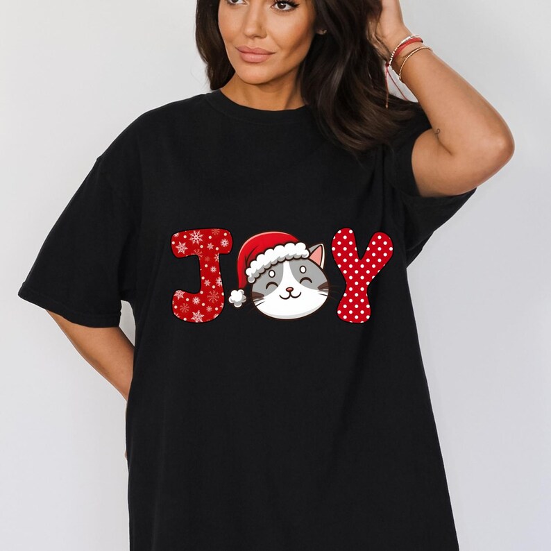 May include: Black t-shirt with a red, white, and gray graphic of the word "JOY" with a cat wearing a Santa hat in the middle of the word.