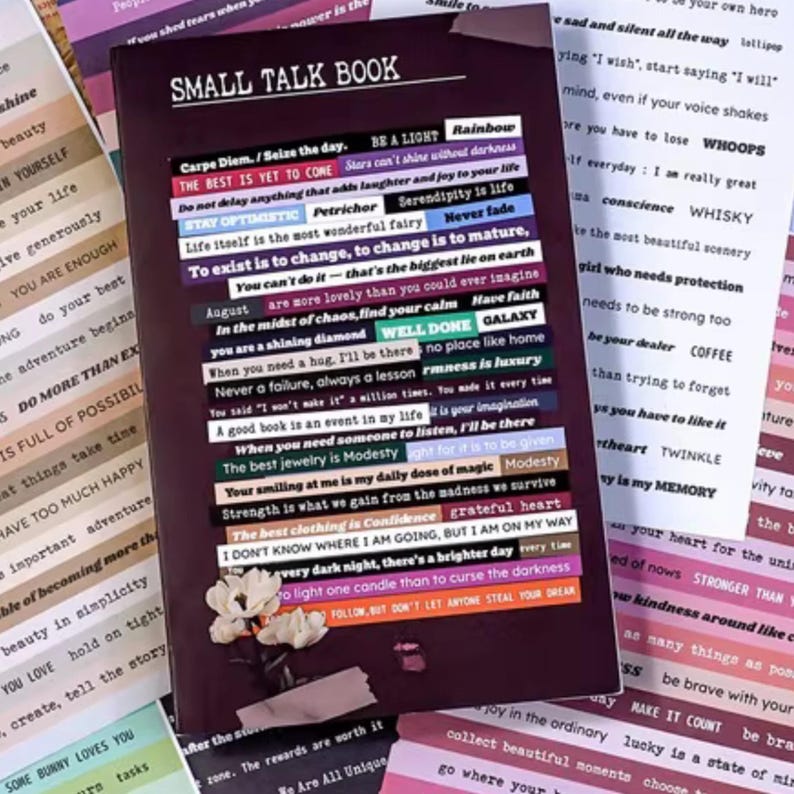 May include: A journal titled "SMALL TALK BOOK" with various colorful sticker quotes. The stickers have phrases like "THE BEST IS YET TO COME" and "YOU ARE ENOUGH". A few small white flowers are at the bottom.