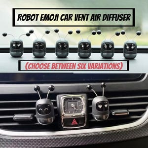 May include: A collection of six gray robot emoji car vent air diffusers with different facial expressions. The text "ROBOT EMOJI CAR VENT AIR DIFFUSER" and "(CHOOSE BETWEEN SIX VARIATIONS)" are displayed above the diffusers.