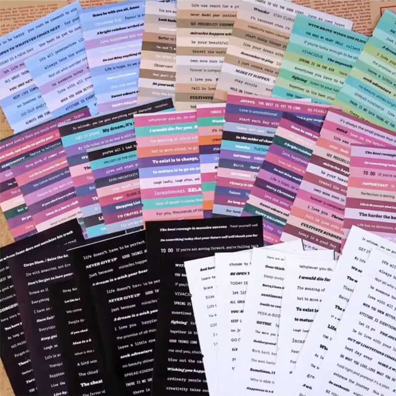May include: A collection of colorful sticker sheets with various inspirational quotes and phrases. The stickers feature a mix of colors, including pink, purple, blue, and black, with white text. The sheets are arranged on a neutral background.