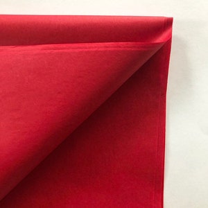 May include: Red tissue paper folded in half, showing the smooth, bright red color.