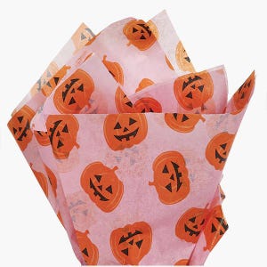 May include: A stack of light pink tissue paper sheets featuring a repeating pattern of orange jack-o'-lanterns with black triangular eyes, noses, and jagged mouths. The thin, translucent paper is folded and fanned out to display the print.