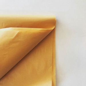 May include: A sheet of light brown tissue paper folded in half. The paper is smooth and has a slightly crinkled texture.