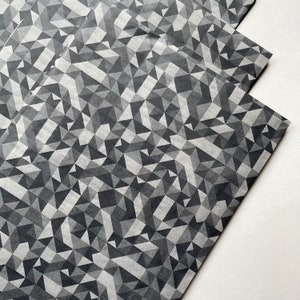 May include: Geometric patterned wrapping paper in shades of gray and white. The design features a repeating pattern of triangles, creating a modern and abstract look. The paper is slightly translucent, with a matte finish.