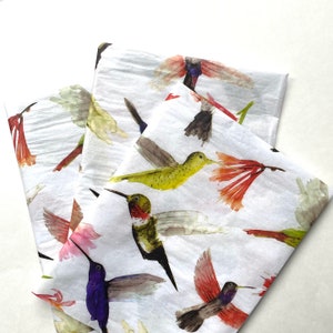 May include: A stack of white tissue paper with a hummingbird pattern. The hummingbirds are painted in watercolor and feature a variety of colors, including green, red, purple, and yellow.
