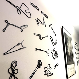 May include: Black metal wall art spelling "King's Island" and depicting roller coaster track layouts. Various shapes and sizes are mounted on a white wall, with a framed black and white print and guitars visible.