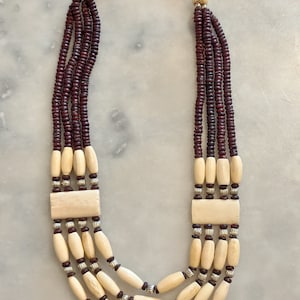 Peut inclure: Un collier multi-rangs composé de perles brunes et blanches. Le collier a un fermoir argenté et est fait de matériaux naturels.