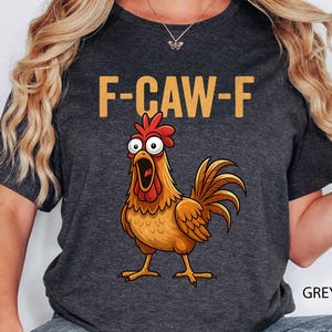 May include: Dark grey heather t-shirt with the text "F-CAW-F" in gold letters above a cartoon rooster with an open beak. The rooster is brown, orange, and red.
