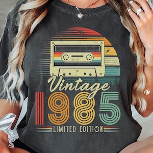 May include: A black t-shirt with a vintage cassette tape design and the text "Vintage 1985 Limited Edition".