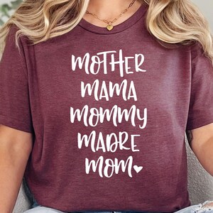 May include: A maroon t-shirt with the words "Mother, Mama, Mommy, Madre, Mom" in white text with a small heart after the word "Mom".