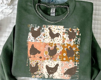 May include: A dark green crewneck sweatshirt featuring a central graphic print of nine square panels. Each panel displays a brown silhouette of a chicken set against a background of various floral patterns in shades of orange, pink, and white.