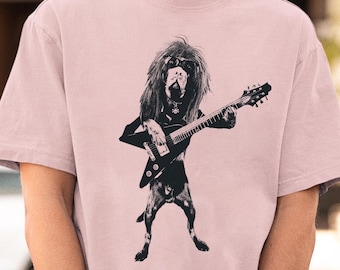 May include: A pink t-shirt with a black and white graphic of a dog playing a guitar. The dog has long hair and is wearing a bandana.