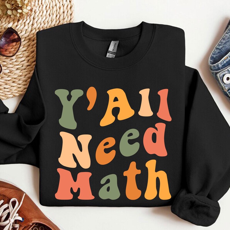 K&ouml;nnte beinhalten: Schwarzer Pullover mit dem Text "Y'all Need Math" in bunter Retro-Schrift.