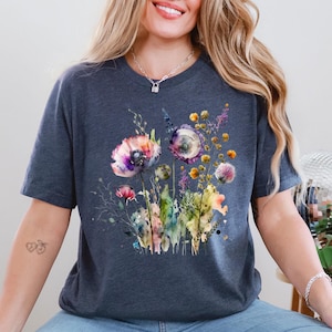 May include: A dark blue t-shirt featuring a watercolor floral design. The design includes colorful flowers in shades of purple, pink, yellow, and green. The flowers are arranged in a bouquet style, with detailed leaves and stems.
