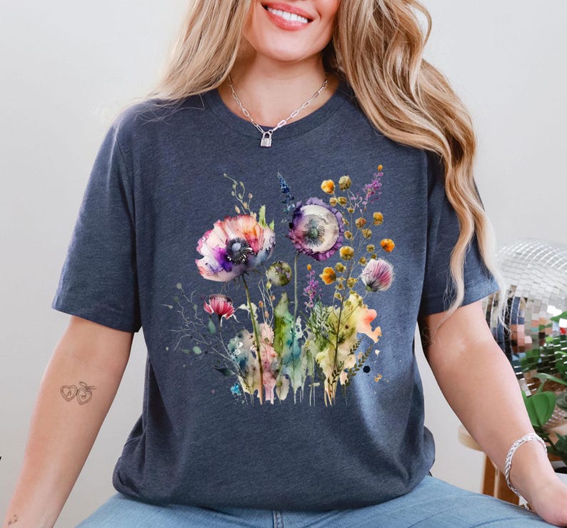 May include: A dark blue t-shirt featuring a watercolor floral design. The design includes colorful flowers in shades of purple, pink, yellow, and green. The flowers are arranged in a bouquet style, with detailed leaves and stems.