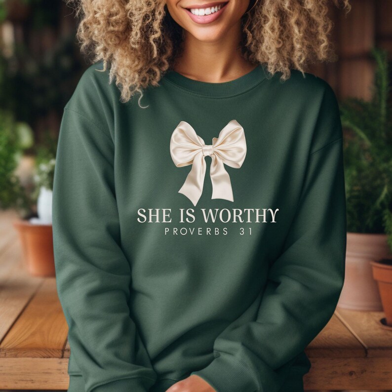 May include: A dark green sweatshirt with a white bow and the text "SHE IS WORTHY PROVERBS 31" printed on the front.