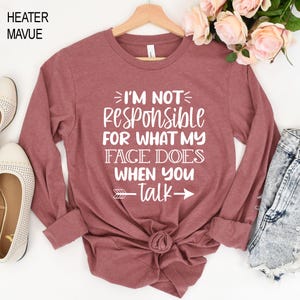 K&ouml;nnte beinhalten: Ein lang&auml;rmeliges, mauvefarbenes T-Shirt mit dem in Wei&szlig; gedruckten Text "Ich bin nicht verantwortlich f&uuml;r das, was mein Gesicht tut, wenn du sprichst". Ein Pfeil zeigt nach rechts neben dem Text.