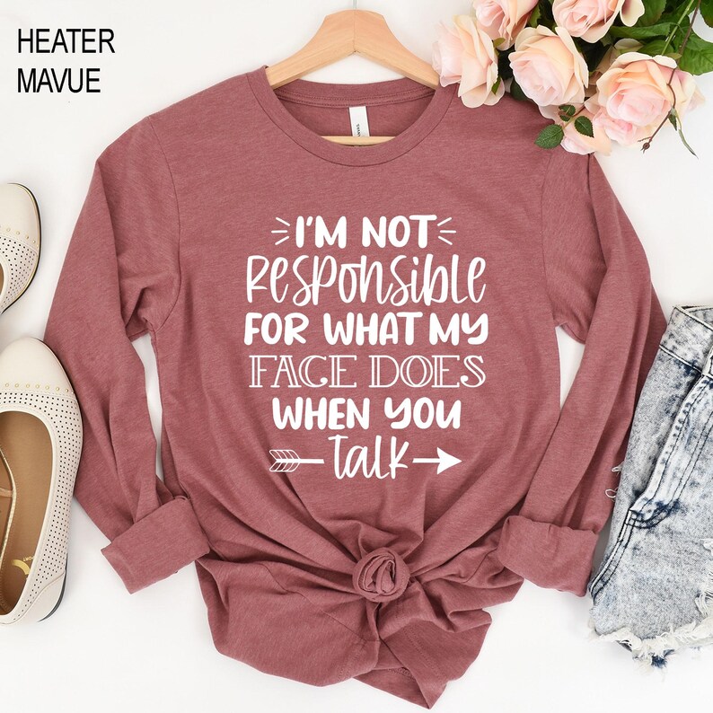 K&ouml;nnte beinhalten: Ein lang&auml;rmeliges, mauvefarbenes T-Shirt mit dem in Wei&szlig; gedruckten Text "Ich bin nicht verantwortlich f&uuml;r das, was mein Gesicht tut, wenn du sprichst". Ein Pfeil zeigt nach rechts neben dem Text.