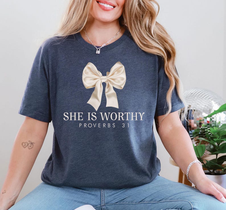 May include: A navy blue t-shirt with a gold bow and the text "She is worthy Proverbs 31" printed on the front.