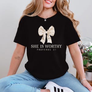 May include: Black t-shirt with a white bow and the text "She is Worthy Proverbs 31" printed on the front.