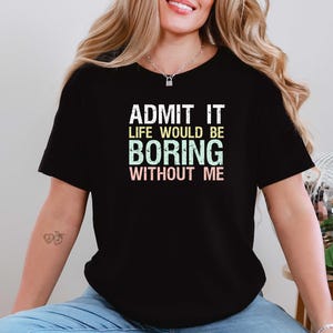 May include: Black t-shirt with the text "ADMIT IT LIFE WOULD BE BORING WITHOUT ME" in white, green, and pink. The shirt is a casual style, suitable for everyday wear.