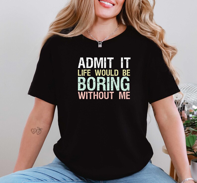 May include: Black t-shirt with the text "ADMIT IT LIFE WOULD BE BORING WITHOUT ME" in white, green, and pink. The shirt is a casual style, suitable for everyday wear.