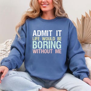 May include: A blue crew neck sweatshirt with the text "ADMIT IT LIFE WOULD BE BORING WITHOUT ME" in white, green, and pink. The sweatshirt is a solid color and has long sleeves.