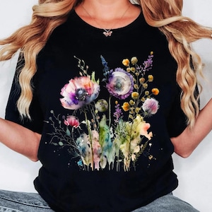 May include: Black t-shirt featuring a watercolor floral design. The design includes pink, purple, yellow, and green flowers and foliage. The flowers are the focal point, with detailed petals and leaves.