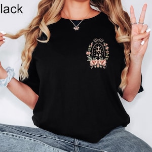 Może przedstawiać: Czarny t-shirt z okrągłym dekoltem z kwiatowym i tekstowym wzorem z przodu. Projekt zawiera krzyż, kwiaty i tekst. Słowo "Black" znajduje się w lewym g&oacute;rnym rogu.