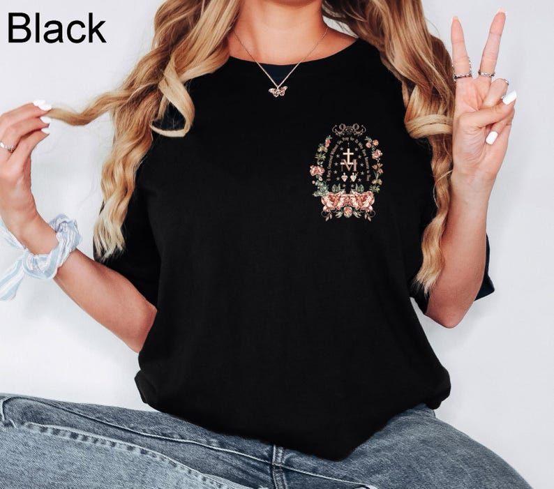 Może przedstawiać: Czarny t-shirt z okrągłym dekoltem z kwiatowym i tekstowym wzorem z przodu. Projekt zawiera krzyż, kwiaty i tekst. Słowo "Black" znajduje się w lewym g&oacute;rnym rogu.