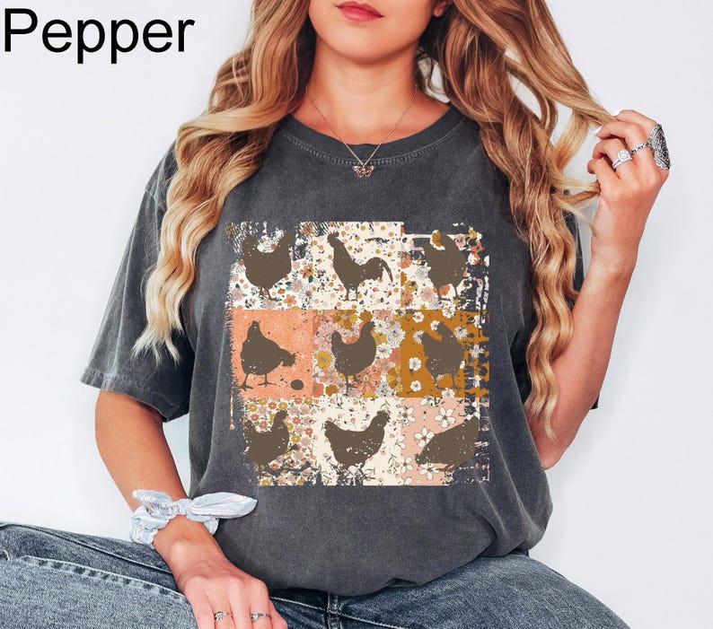 May include: Dark gray t-shirt with a patchwork design featuring chicken silhouettes on a floral background. The word "Pepper" is printed in the upper left corner. The shirt has short sleeves and a relaxed fit.