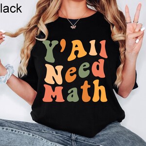 K&ouml;nnte beinhalten: Schwarzes T-Shirt mit dem Text "Y'All Need Math" in bunten, Retro-Lettern.