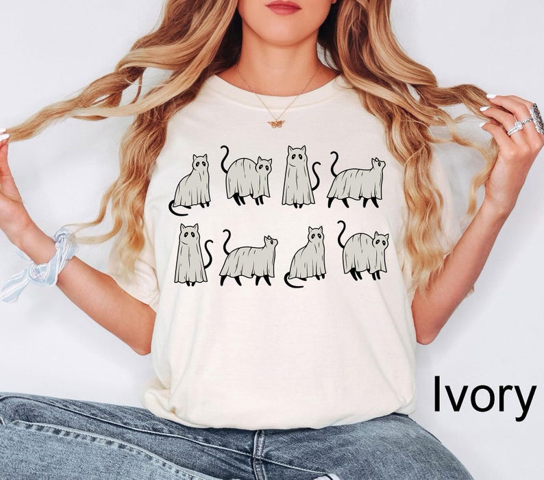 May include: A white t-shirt with a graphic of seven cats dressed as ghosts. The text "Ivory" is in the bottom right corner of the image.